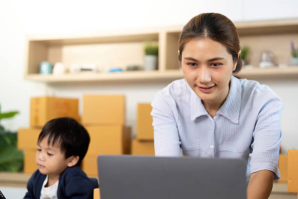 istock Sell Online: A mother focused on her laptop while her child plays nearby 2225539252