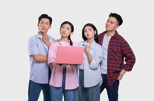 Four young adults pondering a pink laptop screen in front of a white backdrop with thoughtful expressions