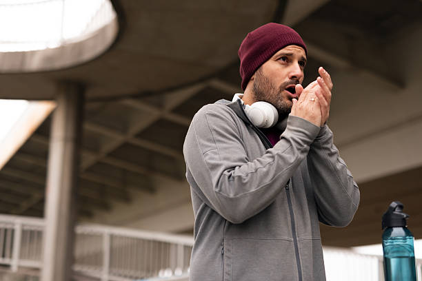 istock Man Warming Hands Outdoors Wearing Headphones and Beanie Hat in Urban Setting 2225549255