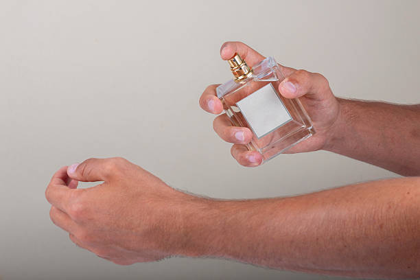 Man spraying perfume on his wrist, holding an elegant glass bottle with blank label