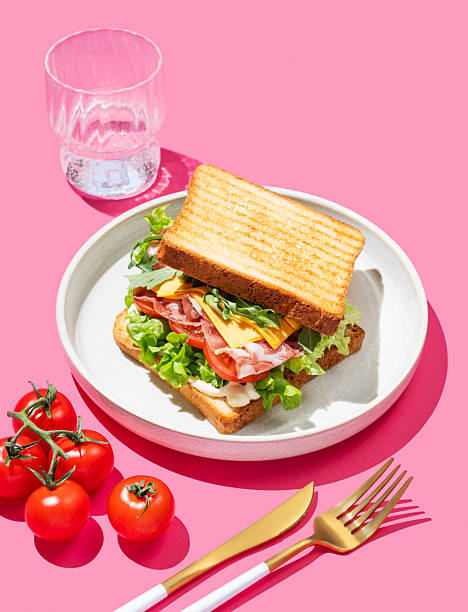 istock Toast bread sandwich with bacon, cheese, tomatoes, lettuce, arugula and sauce on a plate on a pink background 2225553066