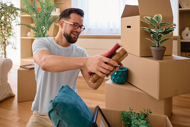 istock Man unpacking books in new home, surrounded by cardboard boxes 2225554181