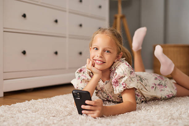 istock Child smiles while relaxing on soft rug and using smartphone at home in cozy 2225554727