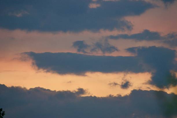 Dramatic evening sky with layered dark clouds and soft pastel hues from the setting sun. A peaceful, moody atmosphere perfect for nature, weather, or twilight-themed visuals.