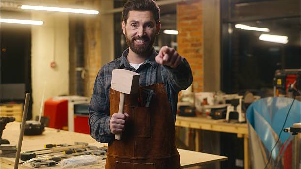 istock Joyful Caucasian carpenter wood master man wave hand come here gesture in workshop repairman architect recruitment craftsman male builder inviting worker holding wooden hammer guy welcoming sign smile 2225562565