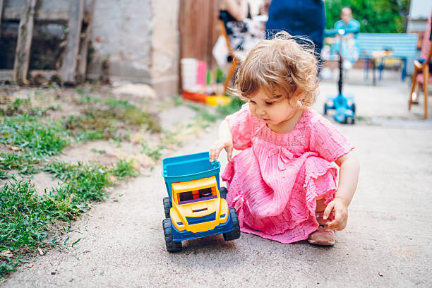 A cheerful little baby girl is playing outdoor. She playing with truck toy.