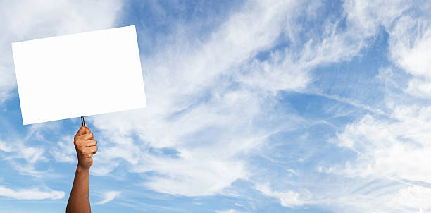 istock Hand holding a blank sign against a blue sky with fluffy clouds during daylight 2225565319