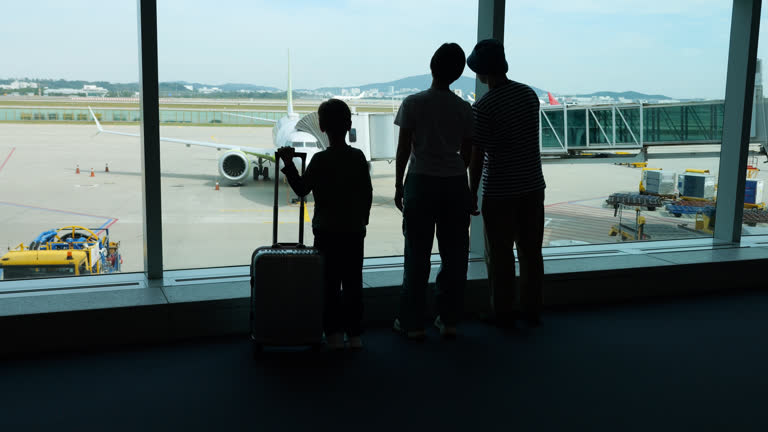Silhouetted family looking to parked airliner and airport grounds from window