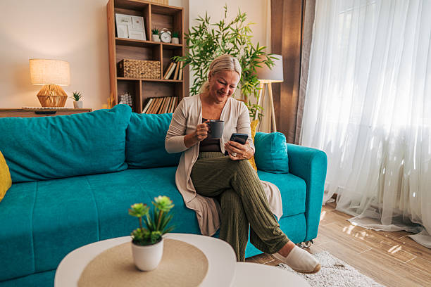 istock Senior woman relaxing on sofa, enjoying coffee and using smartphone at home 2225566594
