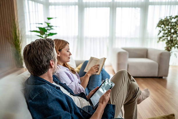 istock Couple relaxing on sofa, reading book and using digital tablet at home 2225572707