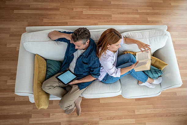 istock Couple relaxing on sofa: woman reading a book, man using a tablet 2225572780