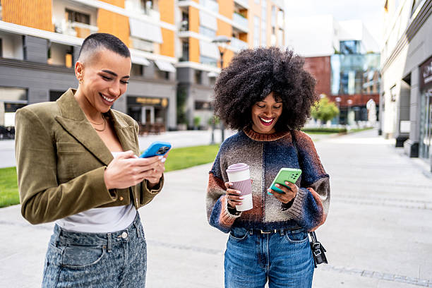 istock Two young women using smartphones while walking in the city 2225588992