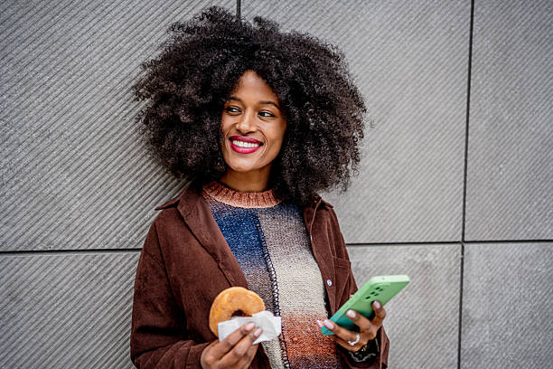 Young woman enjoying a donut and browsing her phone in the city