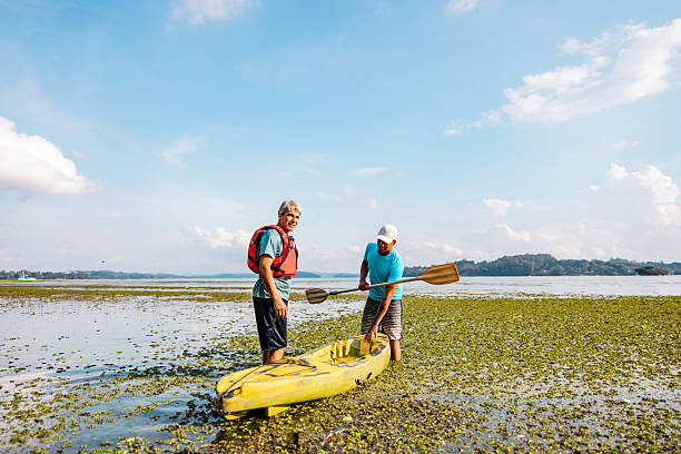 Family time, brother and sister learning to paddle canoe with their father in background.