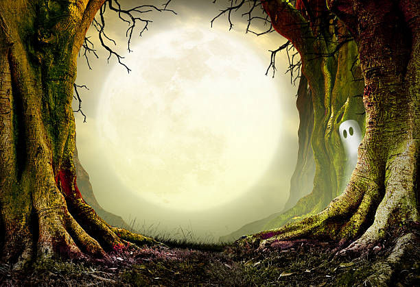 A large rising Halloween moon is framed by spooky and gnarled bare trees as a ghost peers out from behind one of the trees.