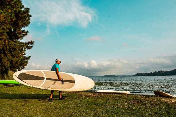 Young man carrying a paddleboard in a lake