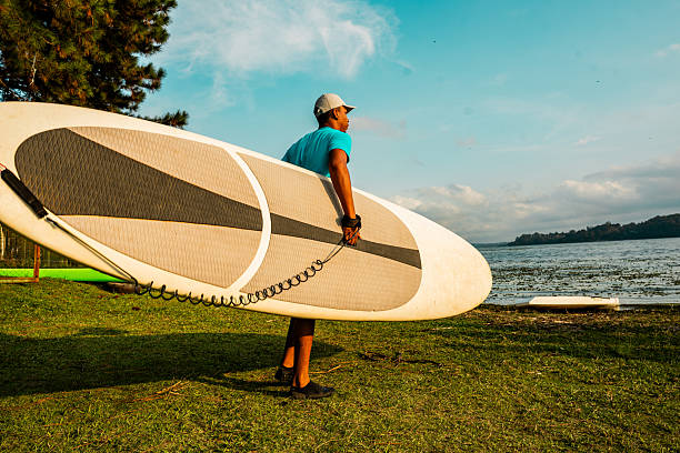 Young man carrying a paddleboard in a lake