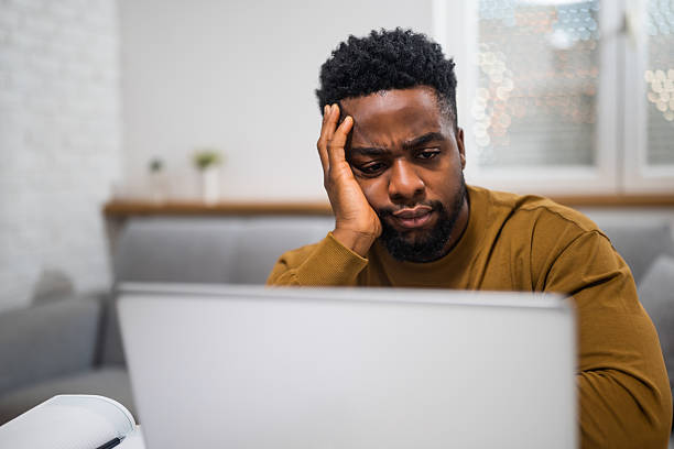 Young African male entrepreneur facing emotional stress and financial failure, working remotely with visible signs of anxiety and frustration.