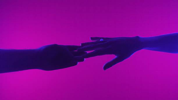 istock Silhouette of Two Hands Reaching Toward Each Other on Pink Background 2225594686