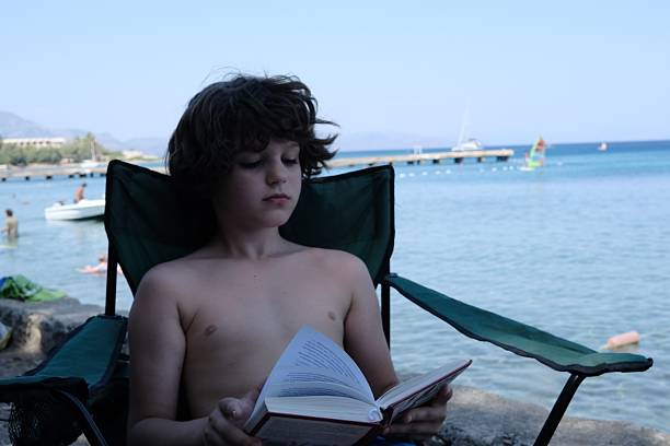 little cute boy with workbook doing homework on table outside in cafe, lifestyle people concept close up