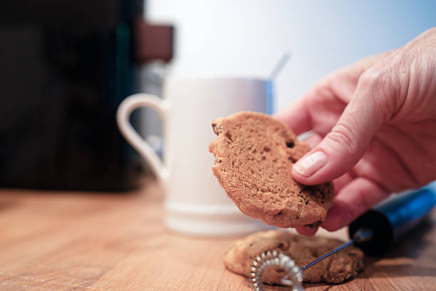 Hand reaching for a freshly baked cookie next to a cup in a cozy kitchen setting