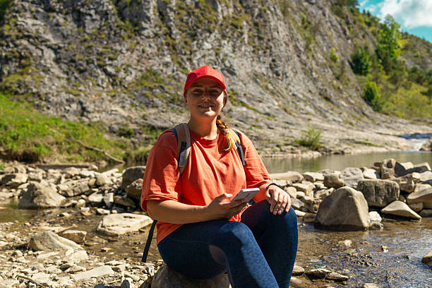 istock Smiling Young Woman Resting by Mountain Stream with Smartphone 2225604916