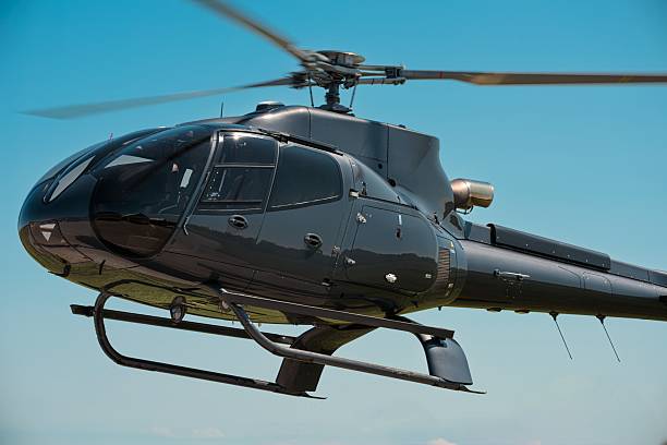 Side view of sleek black helicopter in flight, rotor blades spinning