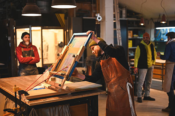 Focused printer preparing screen printing frame in workshop with colleagues