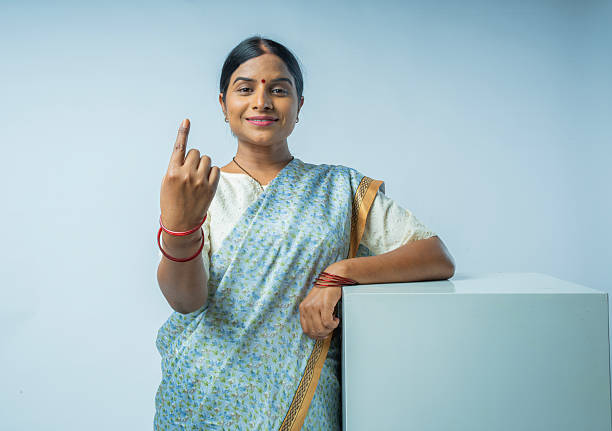 Portrait of young woman in sari showing index finger with voting ink sign while standing over white background