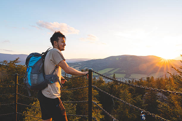 istock Backpacker stands on a platform at golden hour, overlooking the forested hills and valleys of the Jeseniky Mountains bathed in warm sunset light. 2225610303