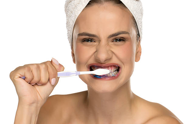istock Young woman fiercely brushing teeth with blue toothpaste, studio shot on white background. 2225616575