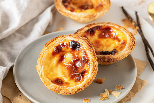 istock Three Pastel de Nata, Portuguese custard tarts, are presented on a plate with cinnamon and vanilla beans. 2225626828
