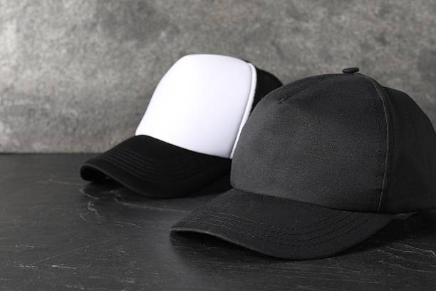 istock Stylish baseball caps on dark textured table, closeup. Mockup for design 2225632541
