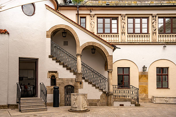 istock Historic Building At Lenbachsplatz In Munich: Elegant Facade With Decorative Gables, Stone Archway, And Red Roof Surrounded By Modern Architecture, Blooming Plants, And Blue Sky With Clouds 2225635912