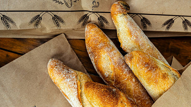 Freshly baked baguettes resting in a paper bag on a wooden table