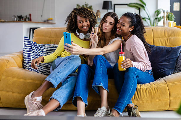 istock Three happy female friends taking selfie on sofa at home 2225640144