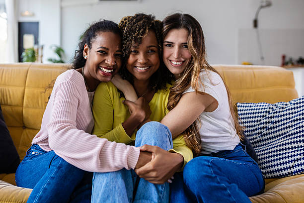istock Three happy female friends embracing on sofa at home 2225640163