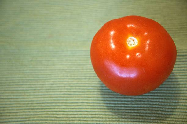 istock One whole red tomato with green background. 2225642054