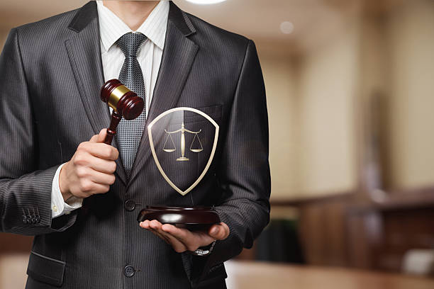 A professional in a suit holds a gavel and a shield with scales of justice. The backdrop features a courtroom, emphasizing the importance of law and justice during proceedings.