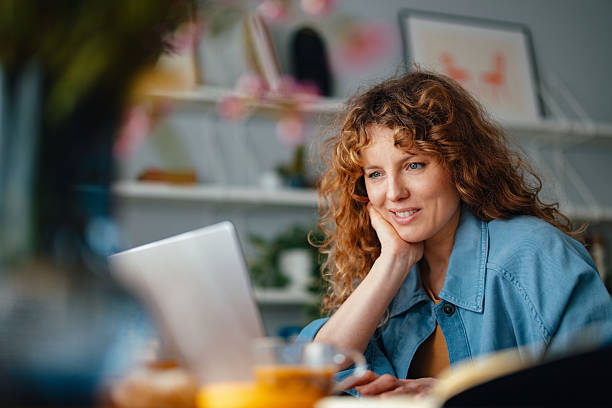 istock Smiling Woman Working on Laptop in a Cozy Home Office Environment 2225648992