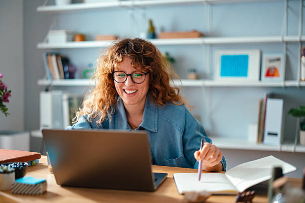 istock Smiling Woman Working in a Home Office with Laptop and Notebook 2225649084