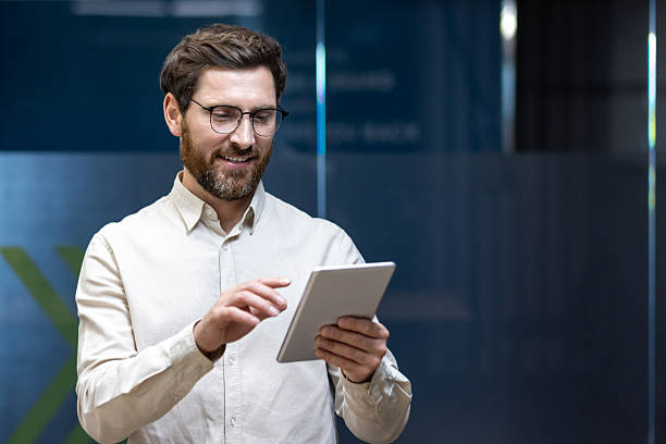 istock Smiling fashionable male programmer, office worker standing indoors and using a tablet in his hands 2225649701