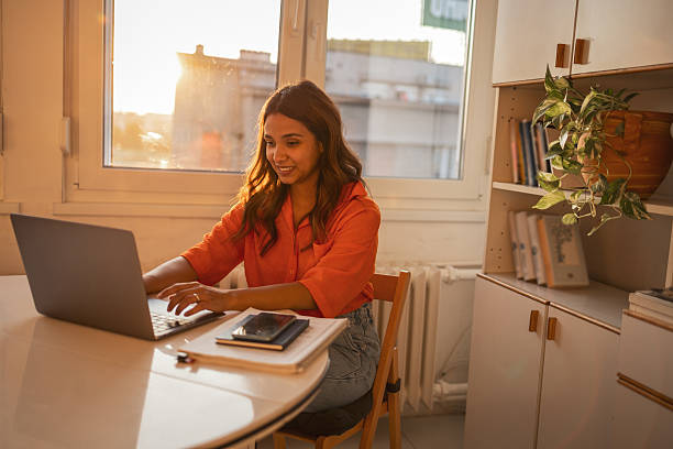 Young woman working from home using laptop at sunset