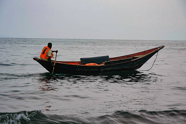 A focused fisherman stands in his boat, skillfully holding a freshly caught fish on the Kafue River, dressed in a light outfit suitable for outdoor activities.