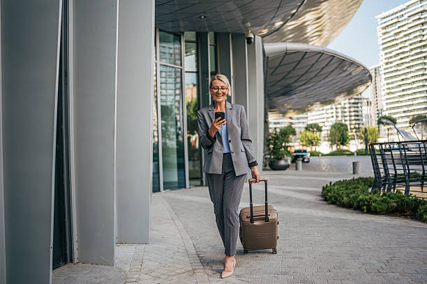 istock Businesswoman walking with suitcase and using smartphone 2225652395