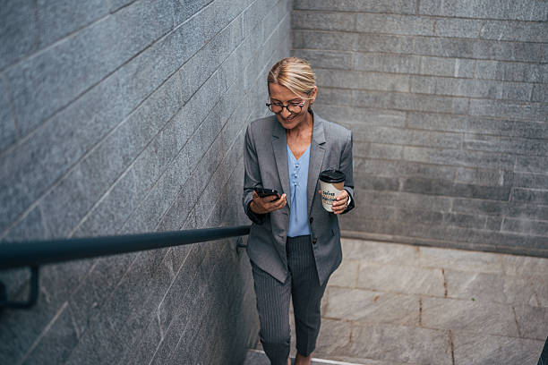 istock Businesswoman walking down stairs while using smartphone and holding coffee 2225654051