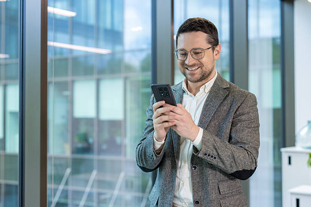 istock A businessman is smiling while checking his phone in a modern office environment. 2225668487