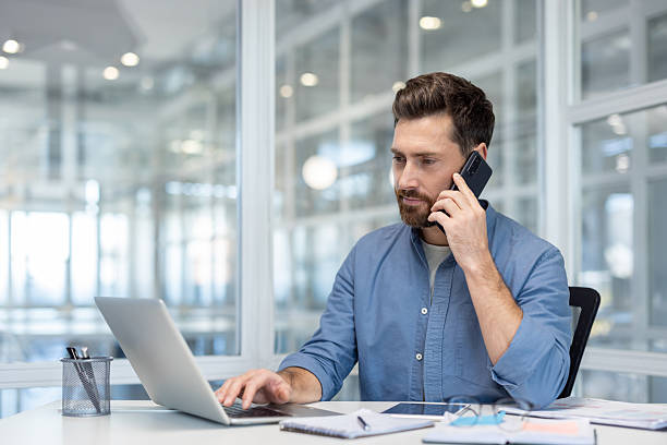 istock A businessman working on a laptop and taking a call in a bright, modern office setting. 2225672285