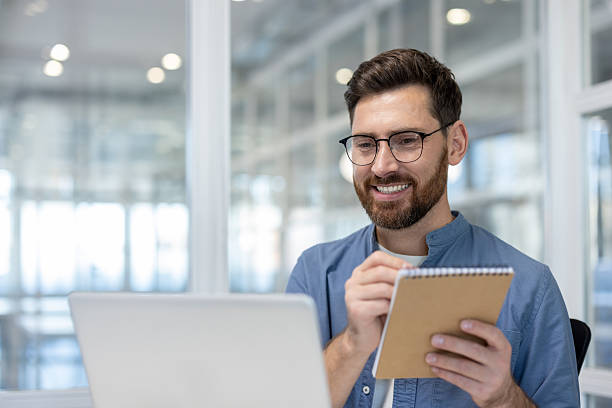 istock Happy man with glasses takes notes while working on a laptop. 2225672412