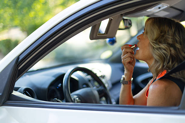 Mature businesswoman is getting ready for a meeting by applying lipstick while sitting in her car